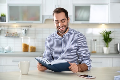 Photo of Handsome young man with cup of coffee reading book at home