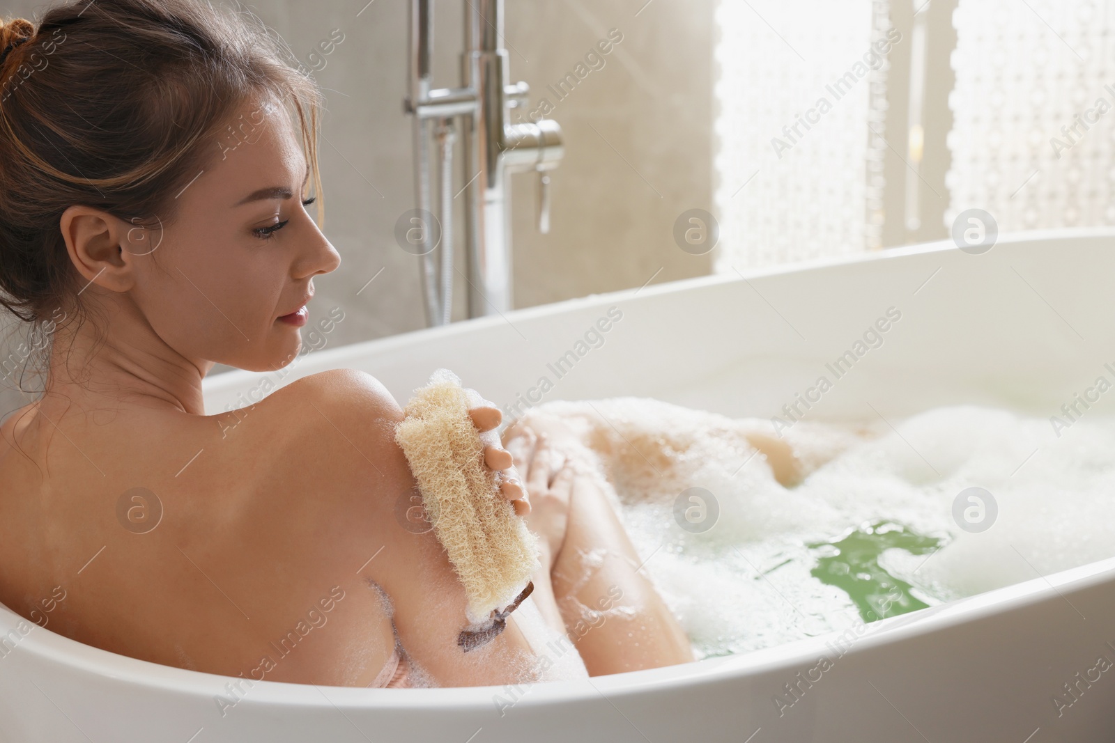 Photo of Beautiful woman with loofah taking bath indoors, space for text