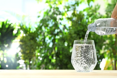 Photo of Pouring water from bottle into glass against blurred background, space for text. Refreshing drink