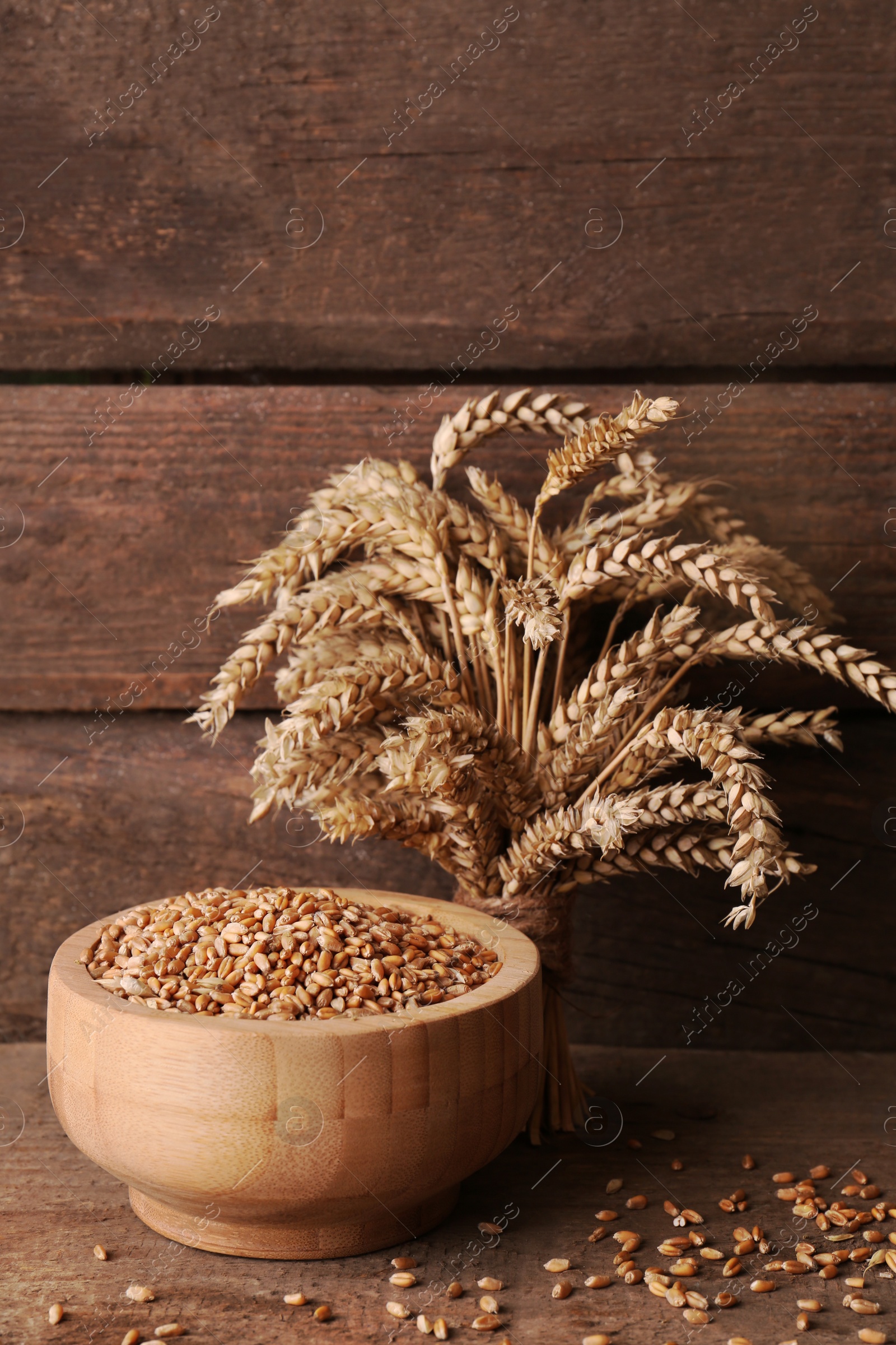 Photo of Wheat grains in bowl and spikes on wooden table