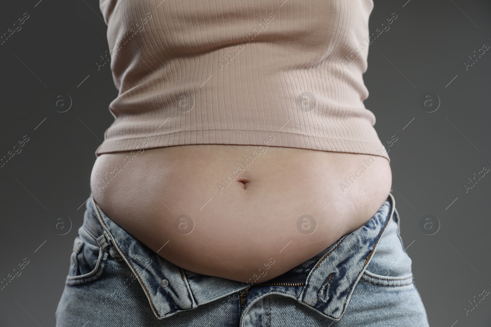 Photo of Woman with excessive belly fat on grey background, closeup. Overweight problem