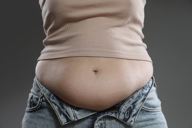 Woman with excessive belly fat on grey background, closeup. Overweight problem