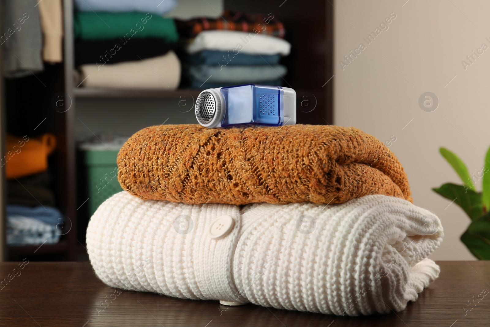 Photo of Fabric shaver and knitted clothes on wooden table indoors