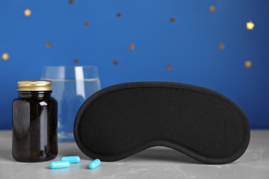 Photo of Sleeping mask and soporific pills on light grey marble table. Bedtime