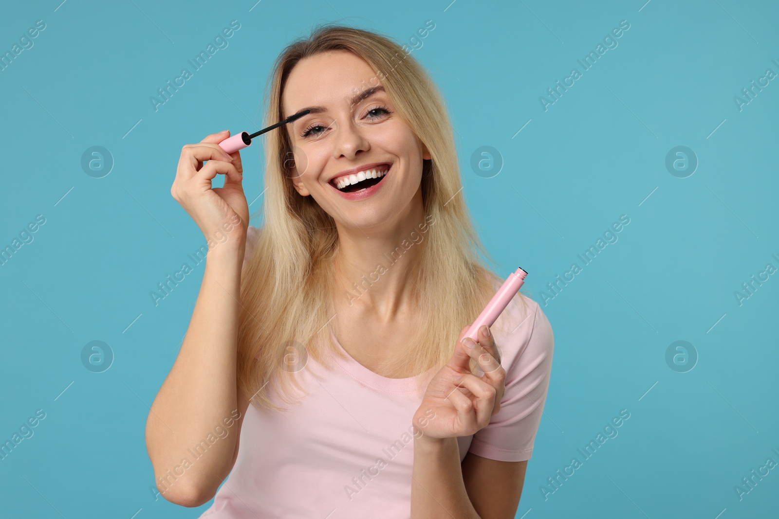 Photo of Beautiful woman applying mascara on light blue background