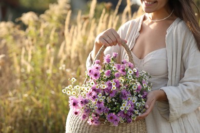 Woman holding wicker basket with beautiful wild flowers outdoors, closeup. Space for text