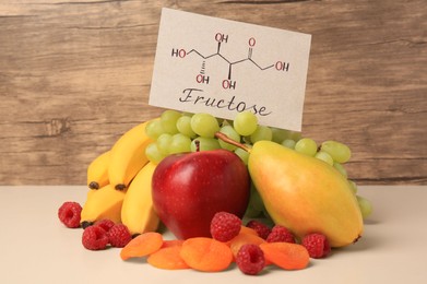 Photo of Card with word Fructose, delicious ripe fruits, raspberries and dried apricots on beige table