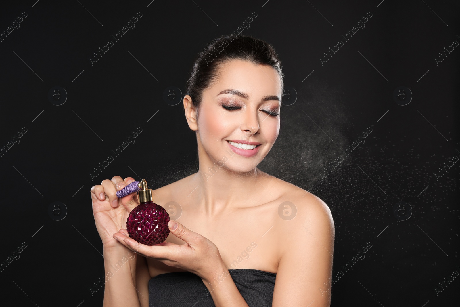 Photo of Young woman spraying perfume on black background