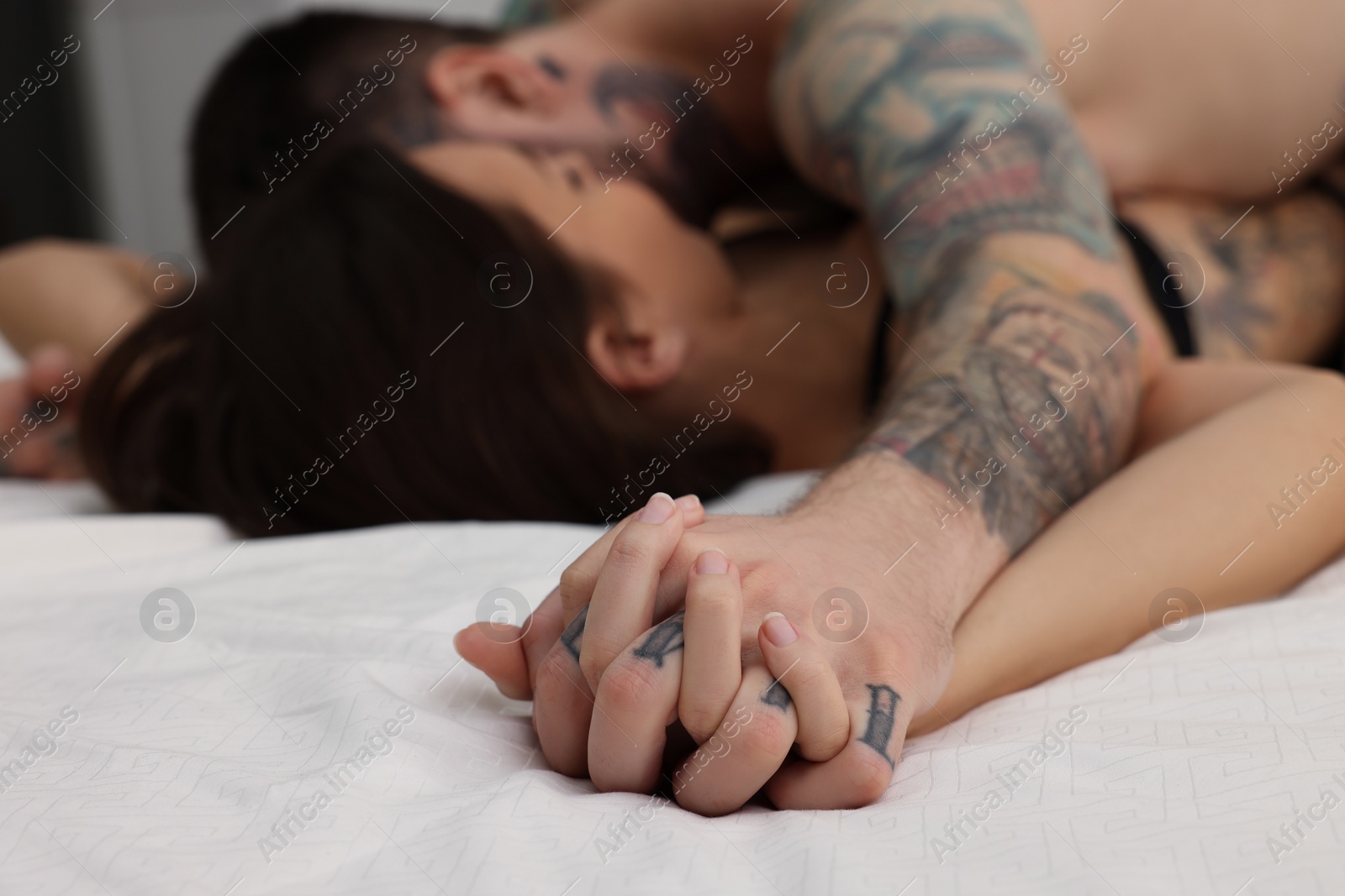 Photo of Passionate couple having sex on bed at home, focus on hands