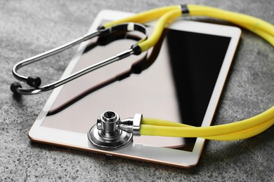 Photo of Modern tablet and stethoscope on grey table, closeup