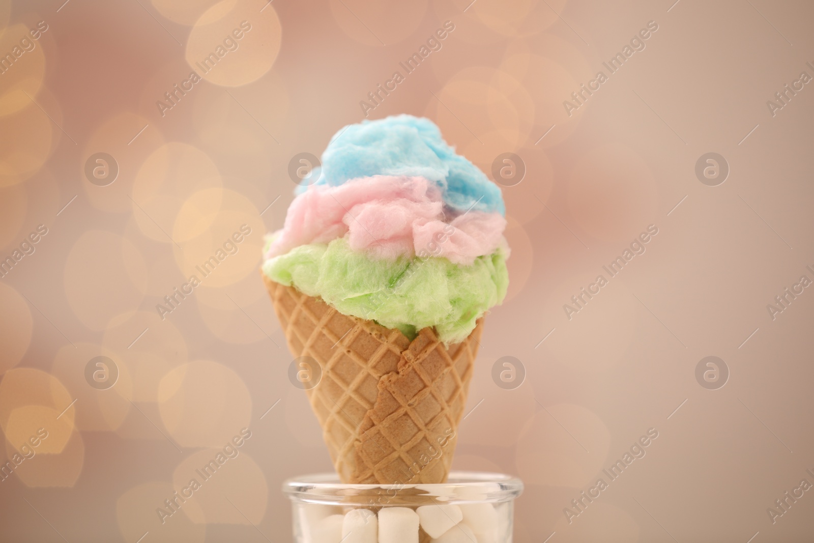 Photo of Sweet cotton candy in waffle cone against blurred lights, closeup