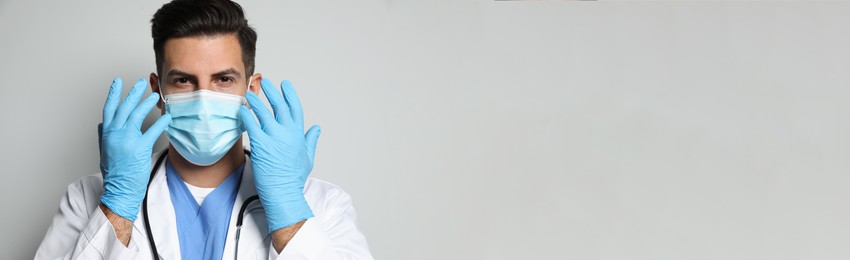 Image of Doctor in protective mask and medical gloves against light grey background. Banner design with space for text 