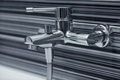 Shiny bath water tap installed on black and white wall