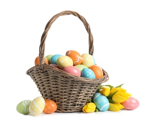 Photo of Wicker basket with painted Easter eggs and spring flowers on white background