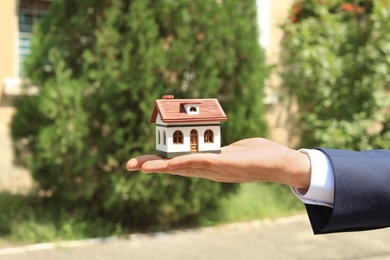 Real estate agent holding house model outdoors, closeup