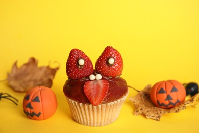 Photo of Delicious cupcake decorated as monster on yellow background. Halloween treat