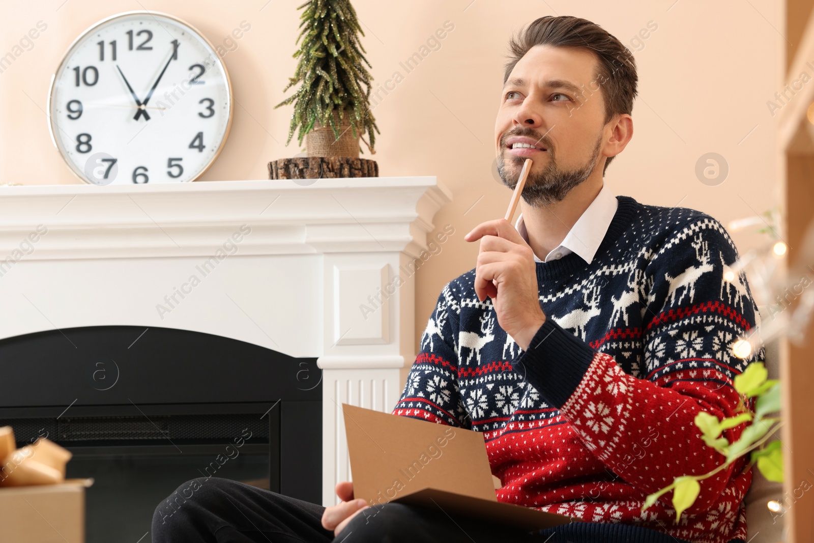 Photo of Man writing wishes in Christmas greeting card in living room