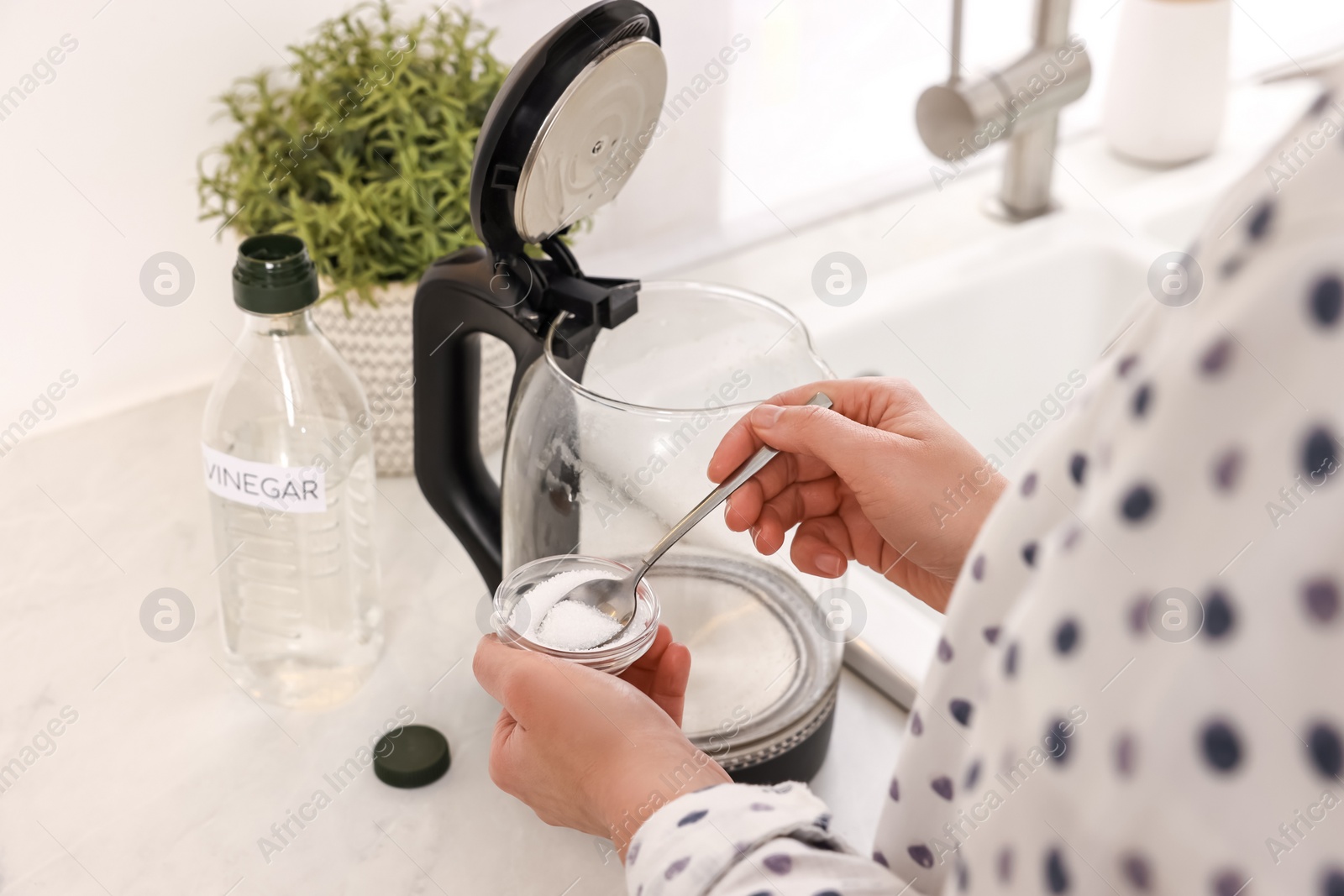 Photo of Woman adding baking soda into electric kettle in kitchen, closeup