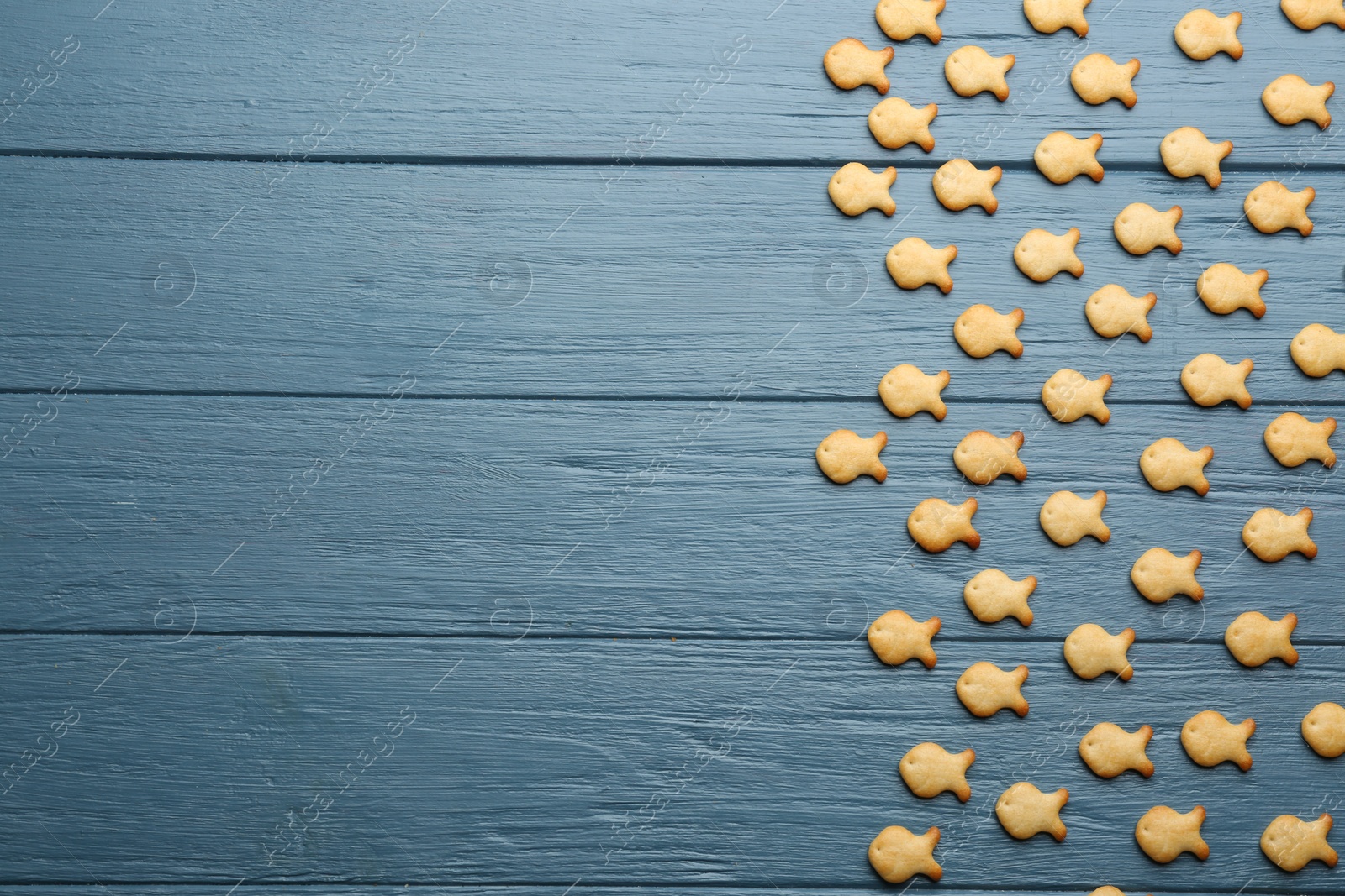 Photo of Delicious goldfish crackers on blue wooden table, flat lay. Space for text