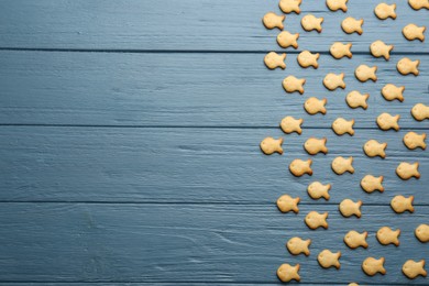 Photo of Delicious goldfish crackers on blue wooden table, flat lay. Space for text