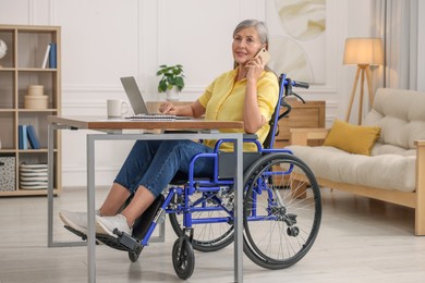 Photo of Woman in wheelchair talking on smartphone at table in home office