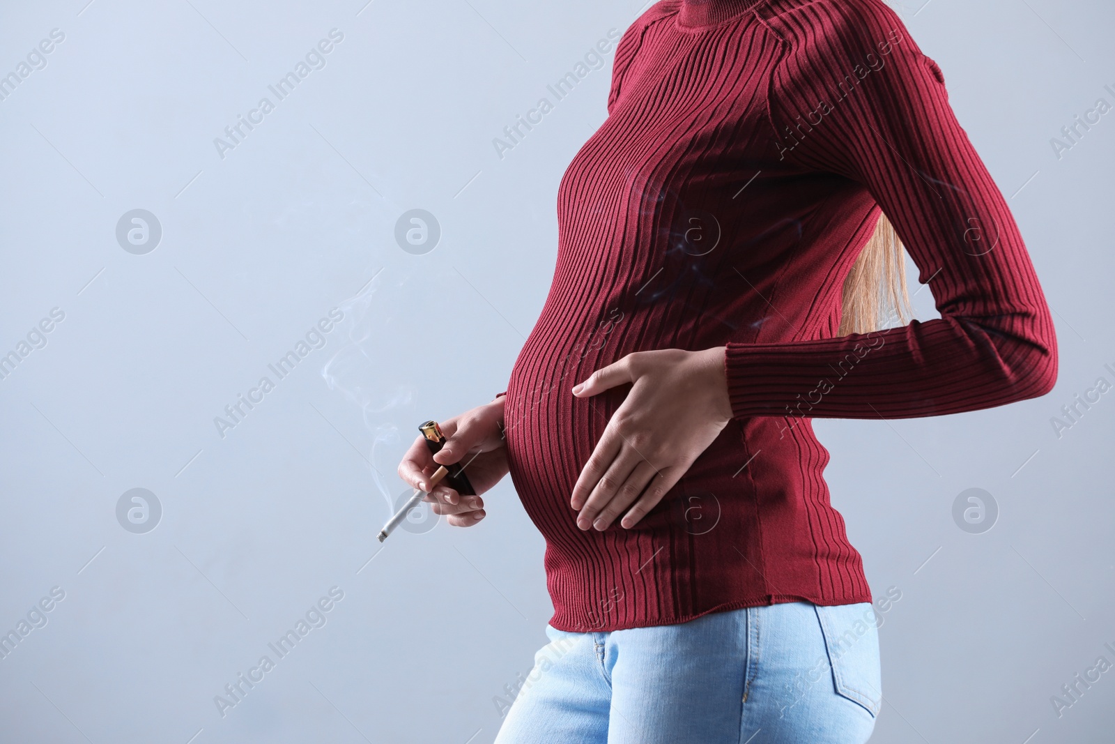 Photo of Young pregnant woman smoking cigarette on grey background, closeup. Space for text