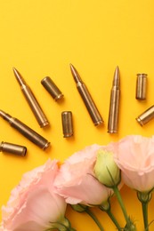 Photo of Bullets, cartridge cases and beautiful eustoma flowers on yellow background, flat lay