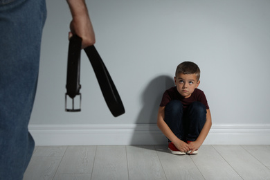 Man threatening his son with belt indoors. Domestic violence concept