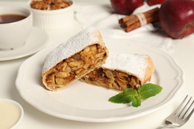 Photo of Delicious strudel with apples, nuts and raisins on white table, closeup