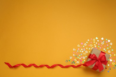 Gift box with sequins on orange background, flat lay. Space for text