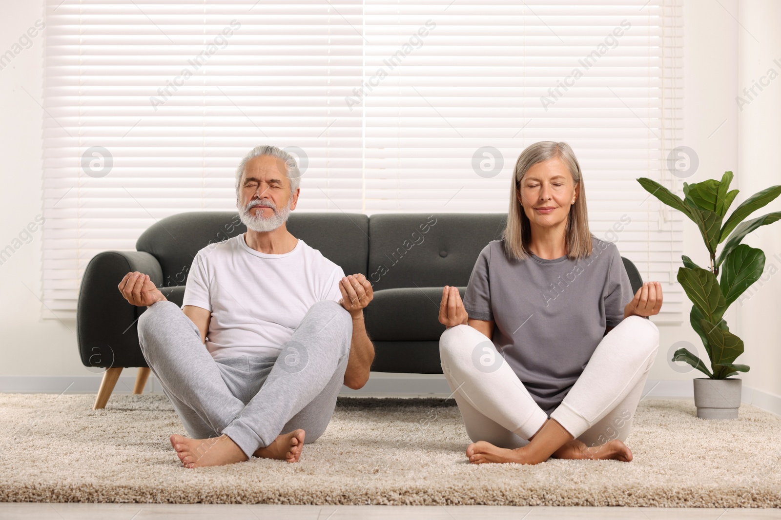 Photo of Senior couple practicing yoga on carpet at home. Healthy lifestyle