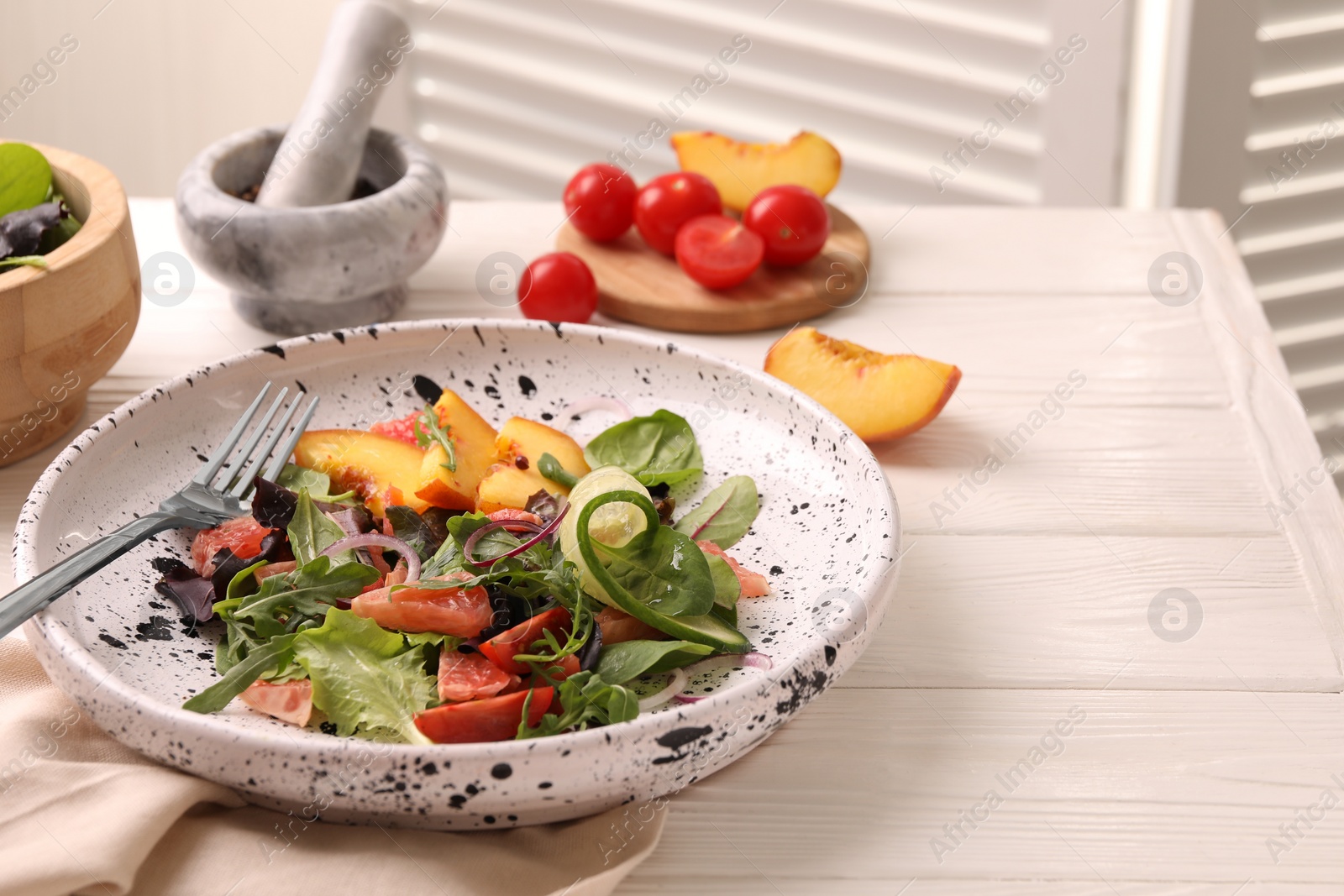 Photo of Delicious salad with vegetables and peach served on white wooden table, space for text