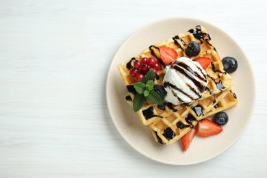 Delicious Belgian waffles with ice cream, berries and chocolate sauce served on white wooden table, top view. Space for text