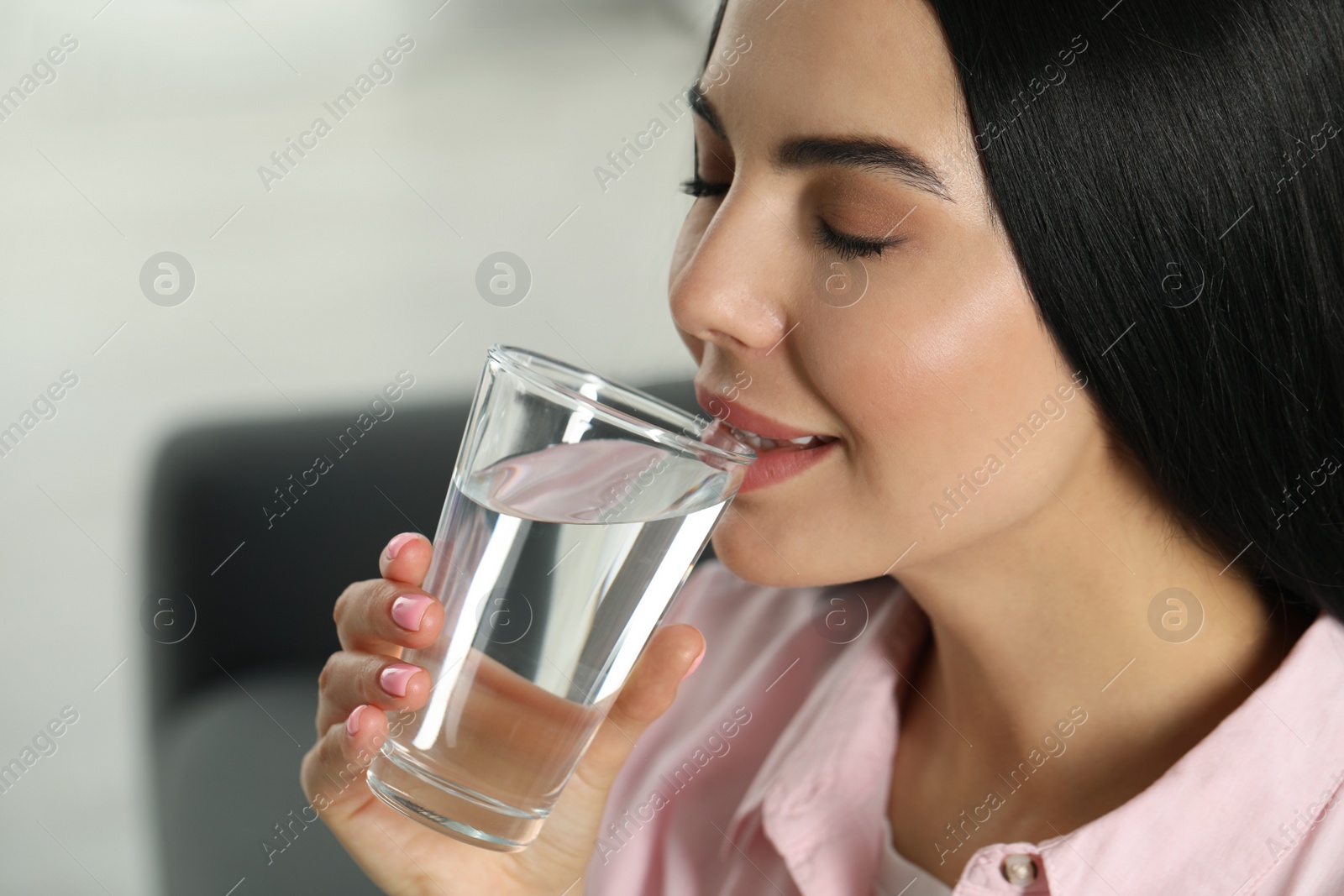 Photo of Young woman drinking water indoors, closeup. Refreshing drink