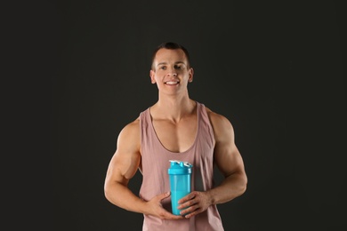 Athletic young man with protein shake on black background