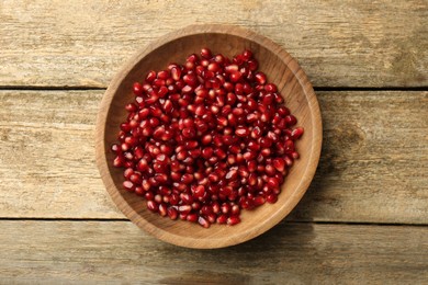 Photo of Ripe juicy pomegranate grains in bowl on wooden table, top view