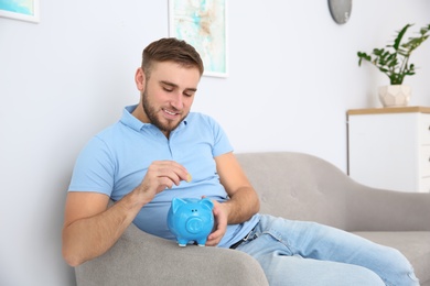 Photo of Young man putting coin into piggy bank in living room
