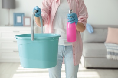 Photo of Woman holding bucket and bottle of cleaning product at home, closeup
