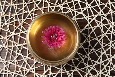 Photo of Tibetan singing bowl with water and beautiful flower on wooden table, top view