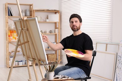 Photo of Man painting in studio. Using easel to hold canvas