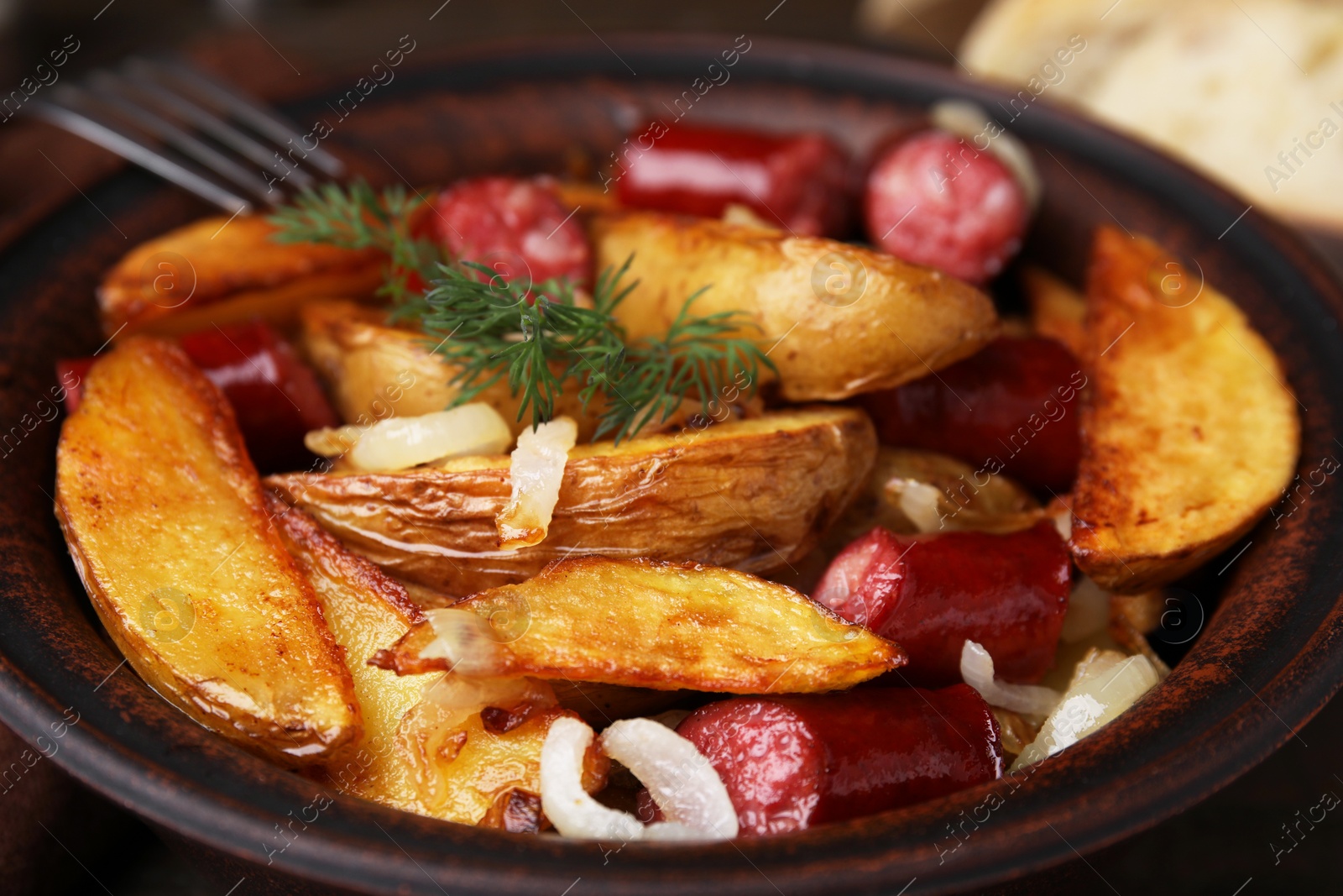 Photo of Delicious baked potato with thin dry smoked sausages and onion in bowl, closeup