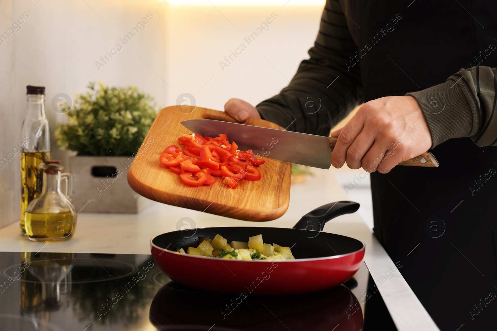 Photo of Cooking process. Man adding cut bell pepper into frying pan in kitchen, closeup