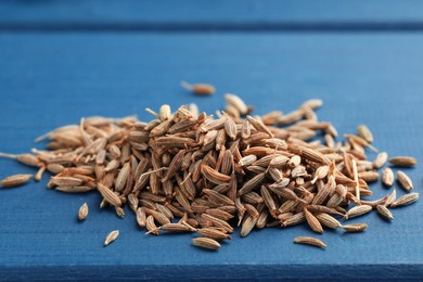 Photo of Pile of caraway seeds on blue wooden table, closeup