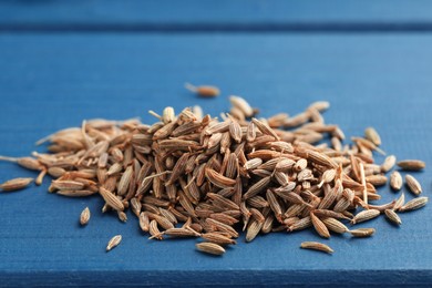 Pile of caraway seeds on blue wooden table, closeup