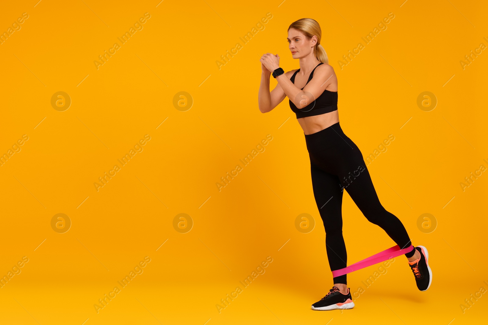 Photo of Woman exercising with elastic resistance band on orange background. Space for text