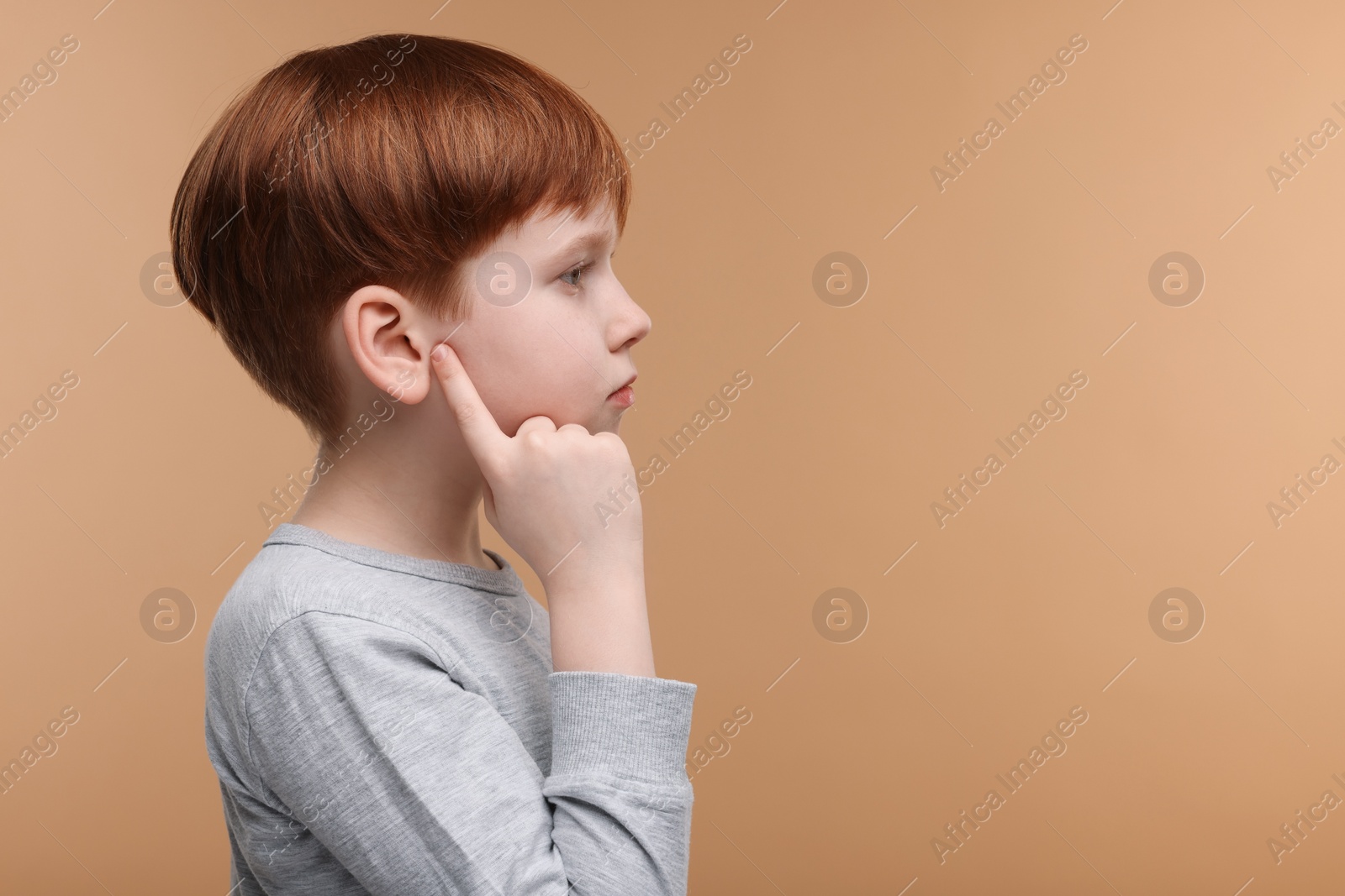 Photo of Little boy with hearing problem on pale brown background, space for text