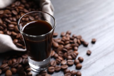 Photo of Shot glass of coffee liqueur and beans on grey table, closeup. Space for text