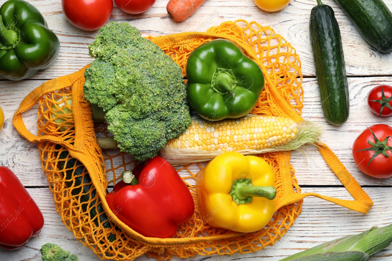 Photo of Net bag with different fresh vegetables on white wooden table, flat lay