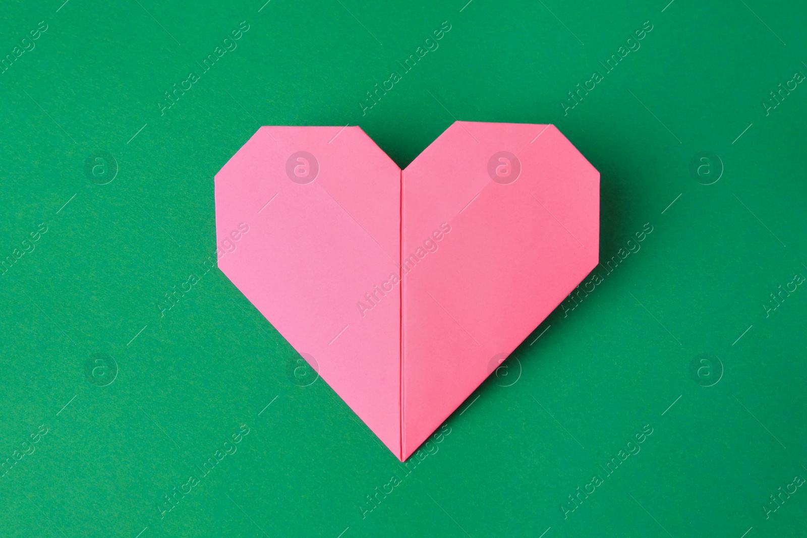 Photo of Origami art. Paper heart on green background, top view