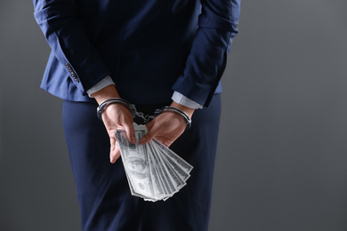 Woman in handcuffs holding bribe money on dark background, closeup